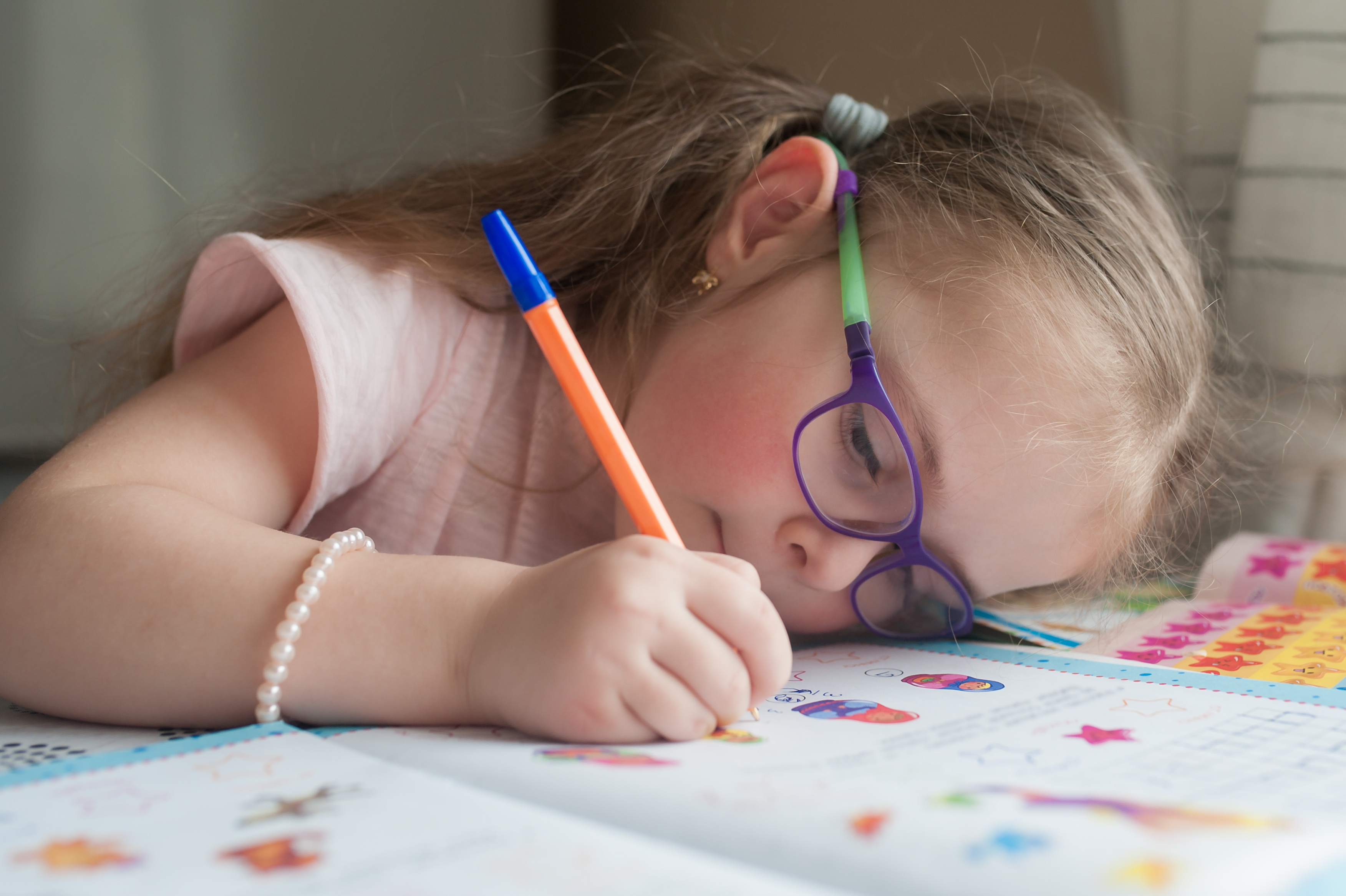 Happy pretty child girls sitting at the table and writes. Educational activities at home. Distance learning. Girl with glasses. Vision problems